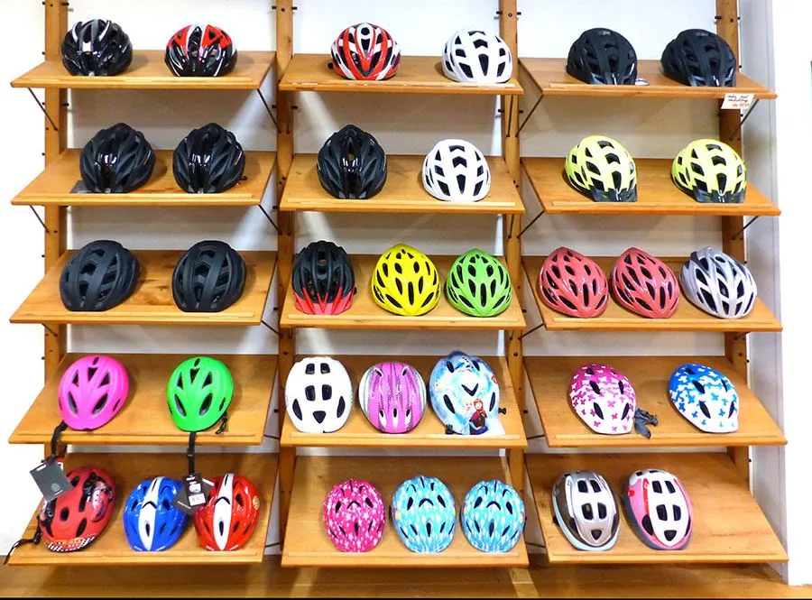 Een wand met fietshelmen in verschillende maten en kleuren, van kinderhelmen tot toerhelmen